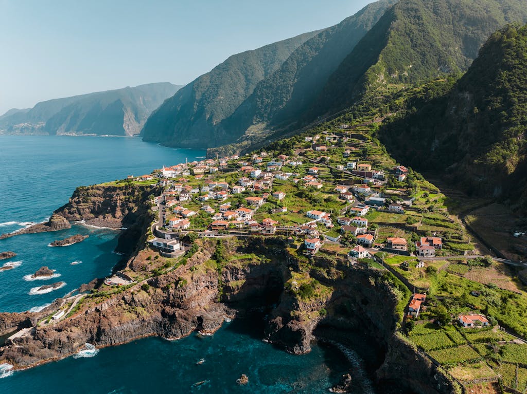Scenic aerial shot of a coastal village in Funchal, Madeira, surrounded by cliffs and ocean.