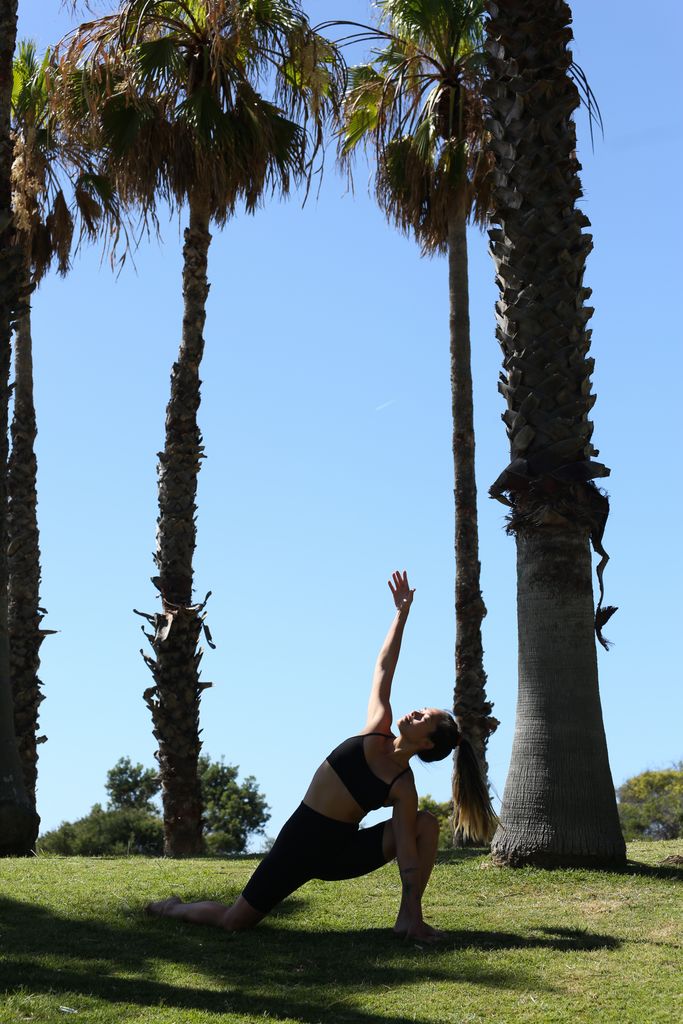 Woman in activewear performing yoga pose under a clear blue sky with palm trees.