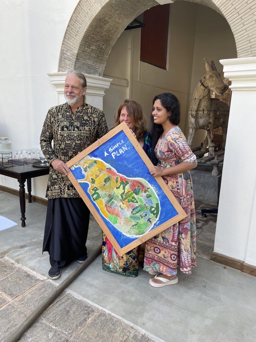 Three people holding a painted map of Sri Lanka titled A Simple Plan