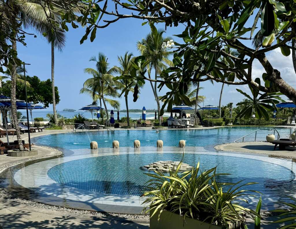 Taj Bentota’s palm-fringed swimming pool with a row of little carved stone elephant fountains, blue umbrellas and sweeping Indian Ocean views