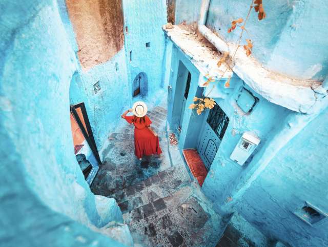 Young woman with red dress visiting the blue city Chefchaouen, Marocco - Happy tourist walking in Moroccan city street - Travel and vacation lifestyle concept